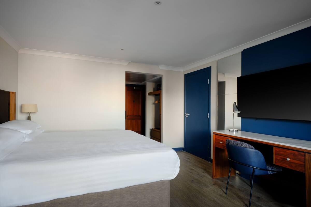 Una habitación de hotel con cama, escritorio, silla, armario y televisor.