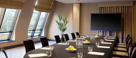 A conference room with a long table, chairs, a potted plant, and a television screen.