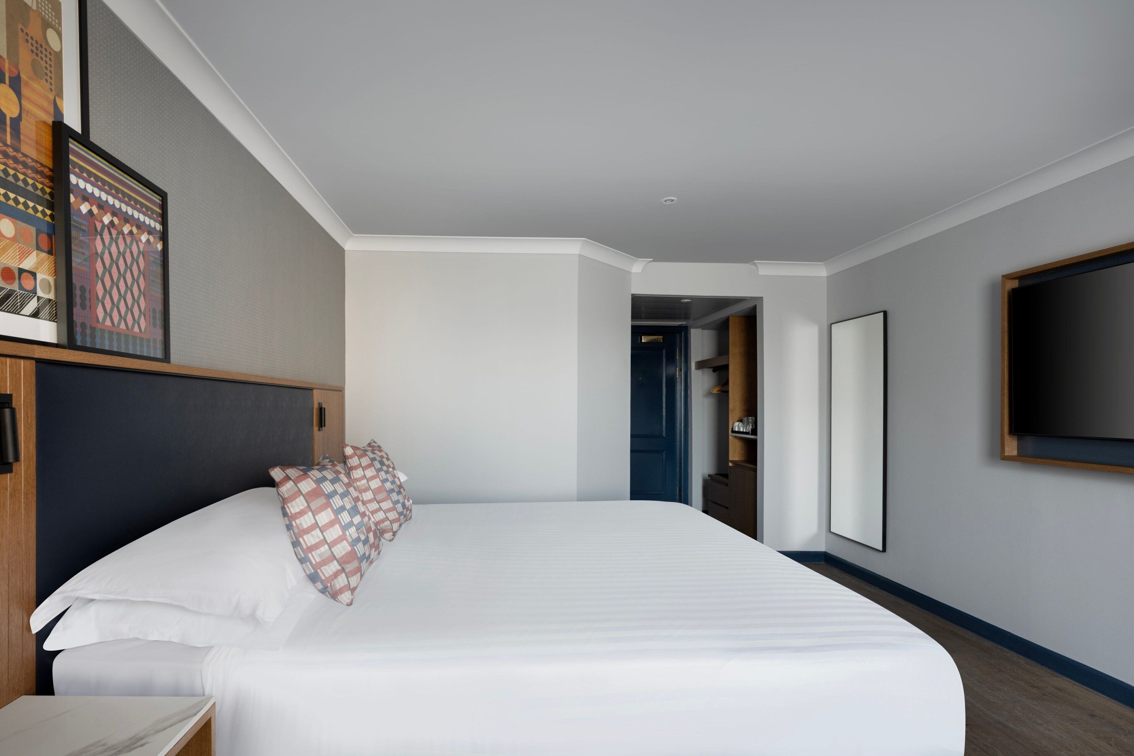 A hotel room with a large bed, a nightstand, a framed picture on the wall, and a door leading to another room.