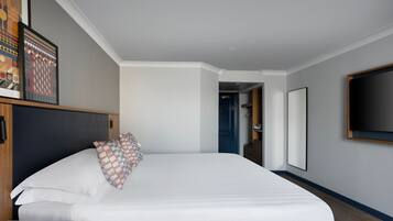 A hotel room with a large bed, a nightstand, a framed picture on the wall, and a door leading to another room.