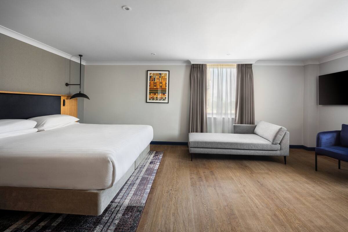 Una habitación de hotel moderna con una cama grande, un sofá, un televisor y una ventana con cortinas.