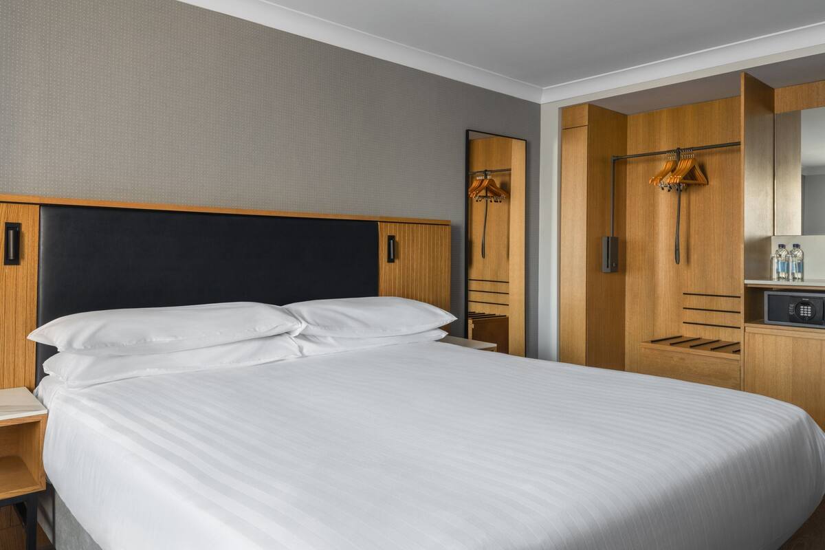 Una habitación de hotel con una cama grande, un armario de madera y un escritorio pequeño con un espejo.