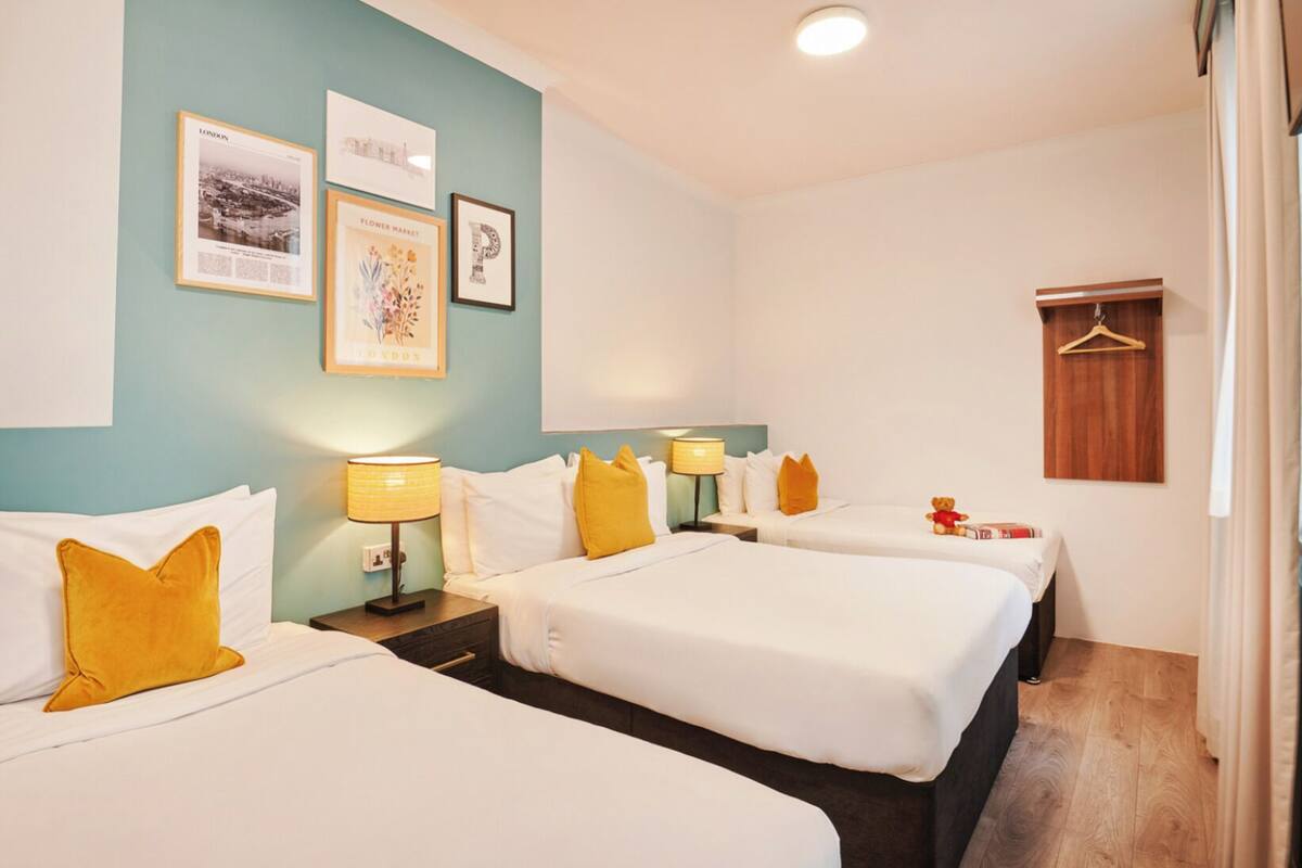 Une chambre d’hôtel avec deux lits, une tête de lit en bois, un porte-manteau mural et des tableaux encadrés accrochés au mur.