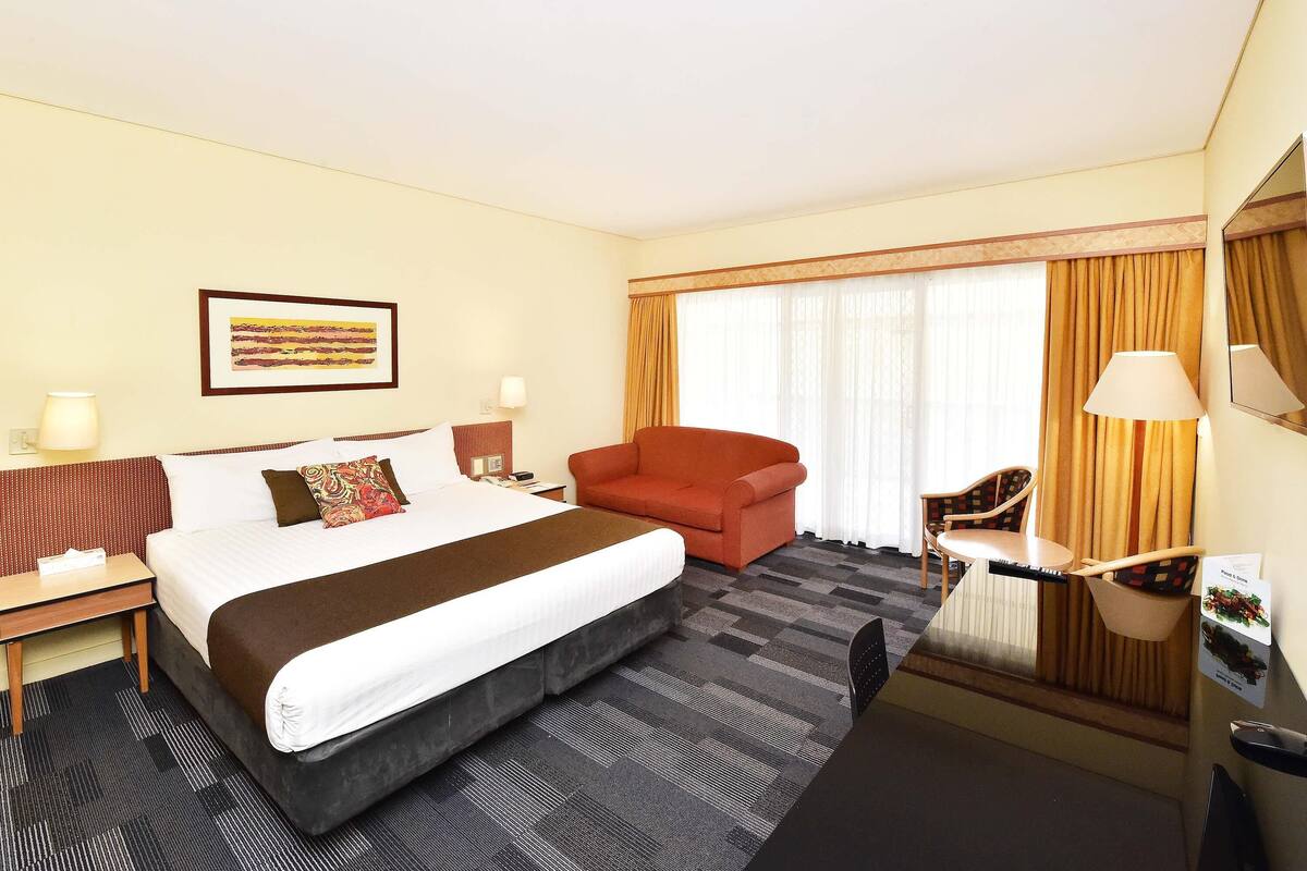 A hotel room with a large bed, a desk, a chair, and a sofa.