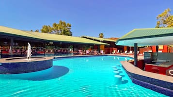 Relax by the resort's pool surrounded by lounge chairs and umbrellas, with a water feature and a covered seating area nearby.