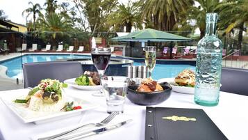 Ein Esstisch mit Mahlzeit, einer Wasserflasche und einem Weinglas, mit Blick auf einen Pool und Palmen.