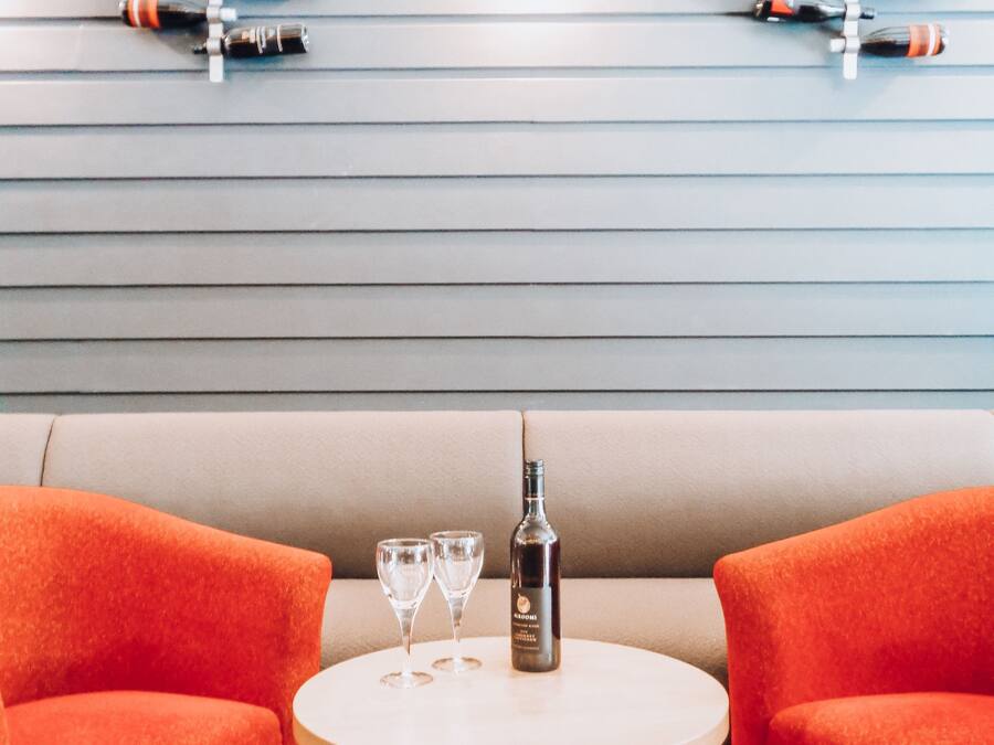 Une pièce comprenant un canapé et deux fauteuils, une table avec une bouteille et des verres, et un mur orné de bouteilles de vin.