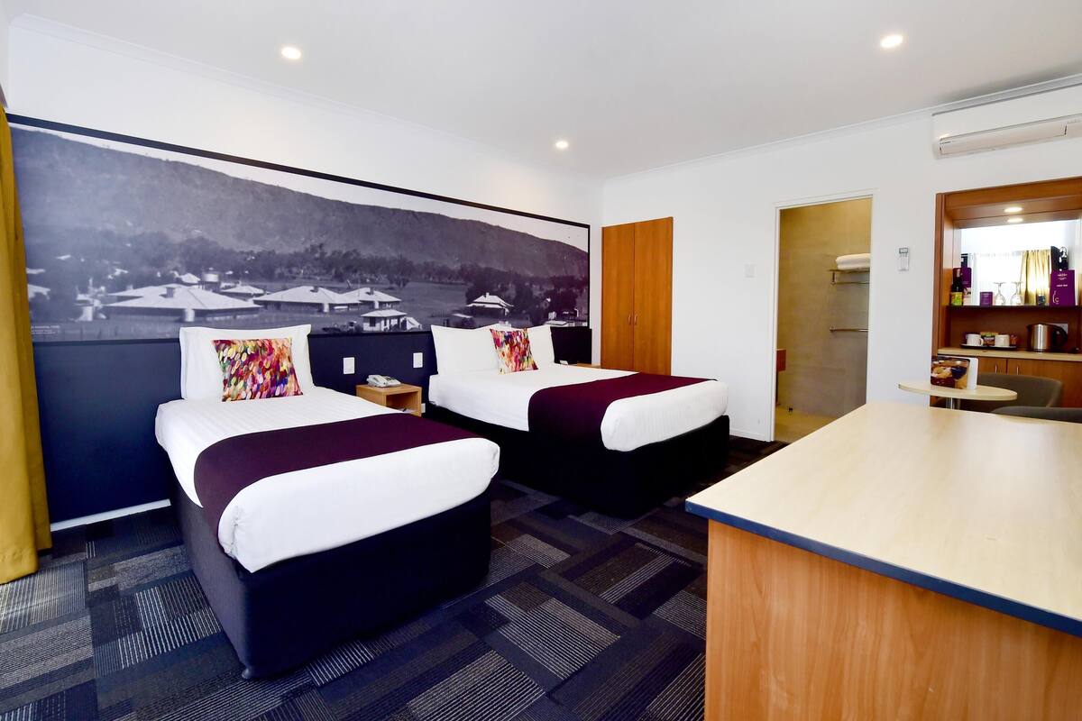 A hotel room with two beds, a desk, and a large window with a view of a landscape.