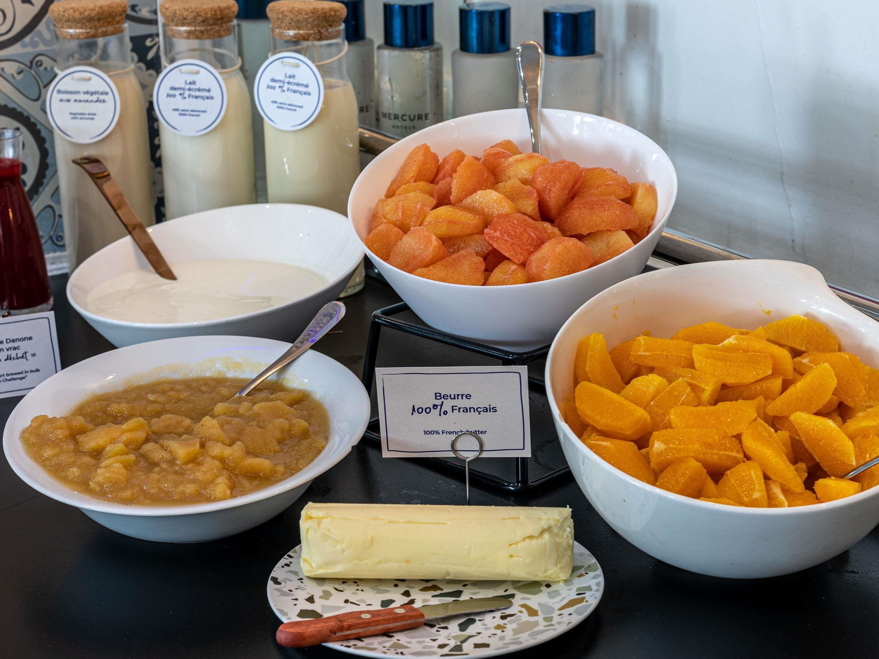 Une table de buffet proposant divers aliments, notamment un bol de soupe, une assiette de beurre, un saladier de fruits et plusieurs bouteilles de lait.