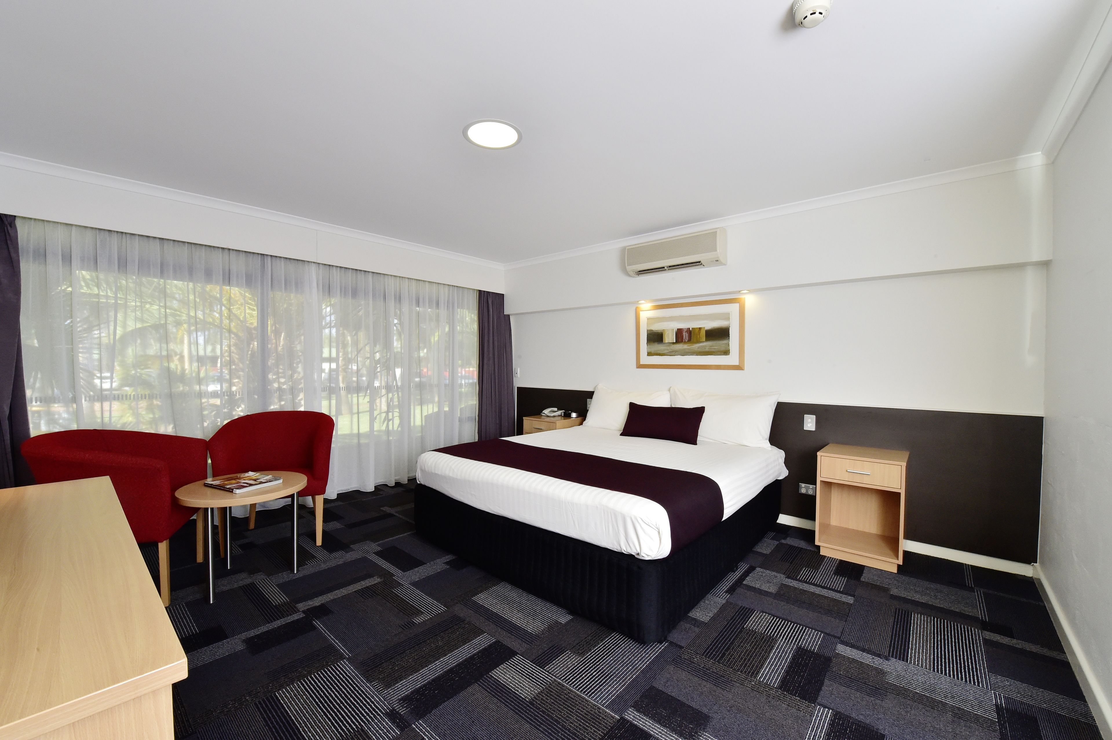 A hotel room with a large bed, a desk, two chairs, and a small table.