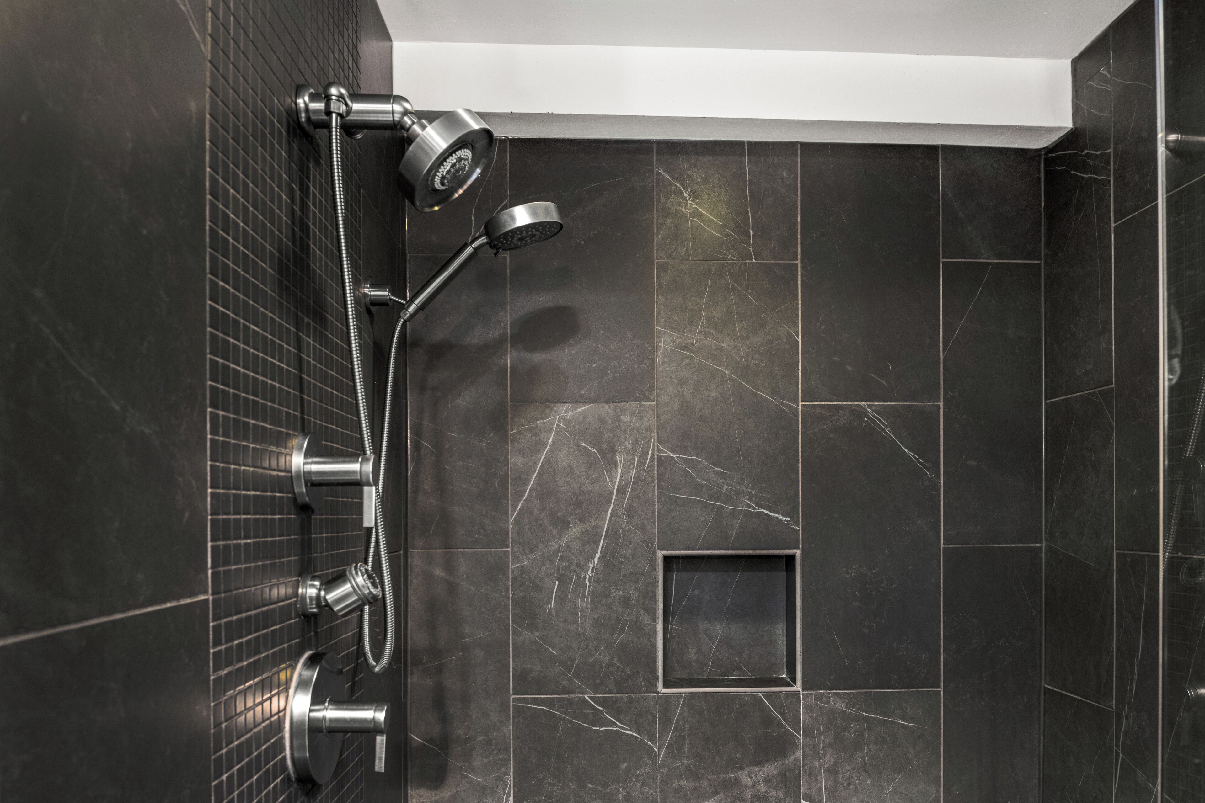 A modern bathroom with a black tiled wall, a shower with a handheld showerhead, and a square tile design.