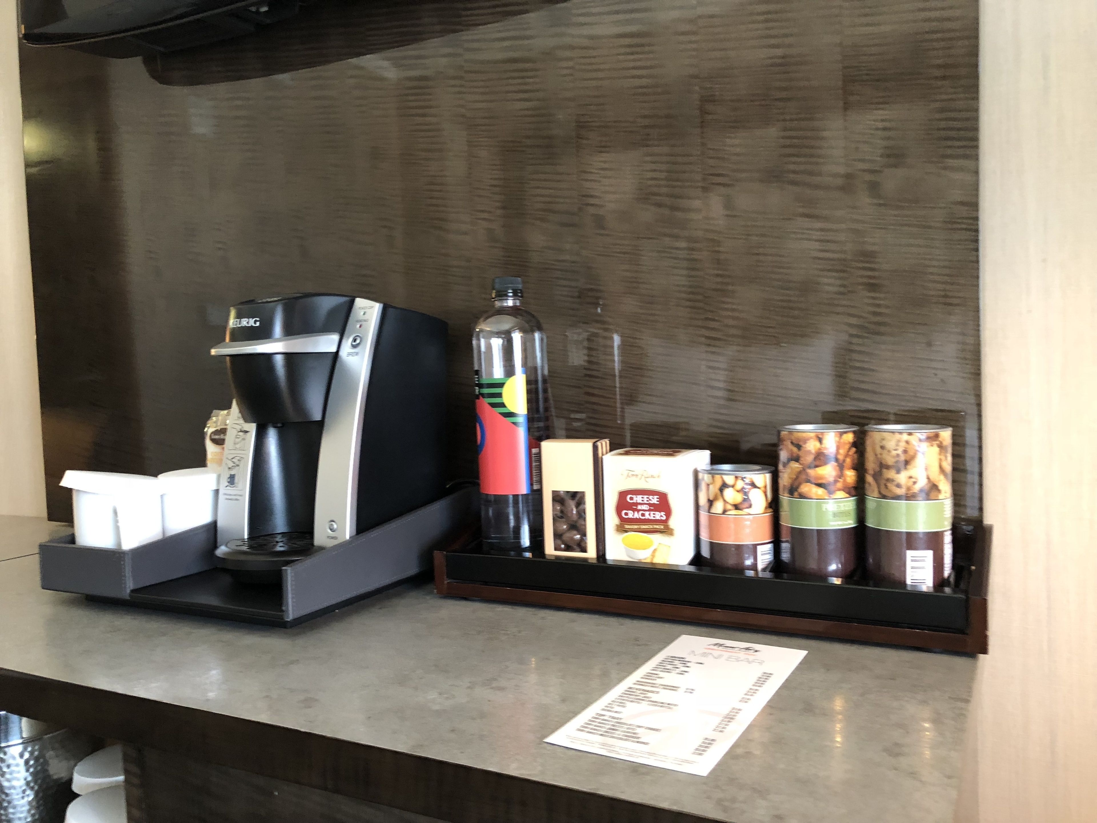 A coffee machine, a bottle of water, and snack containers on a counter.