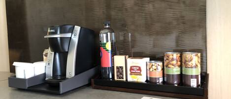 A coffee machine, a bottle of water, and snack containers on a counter.