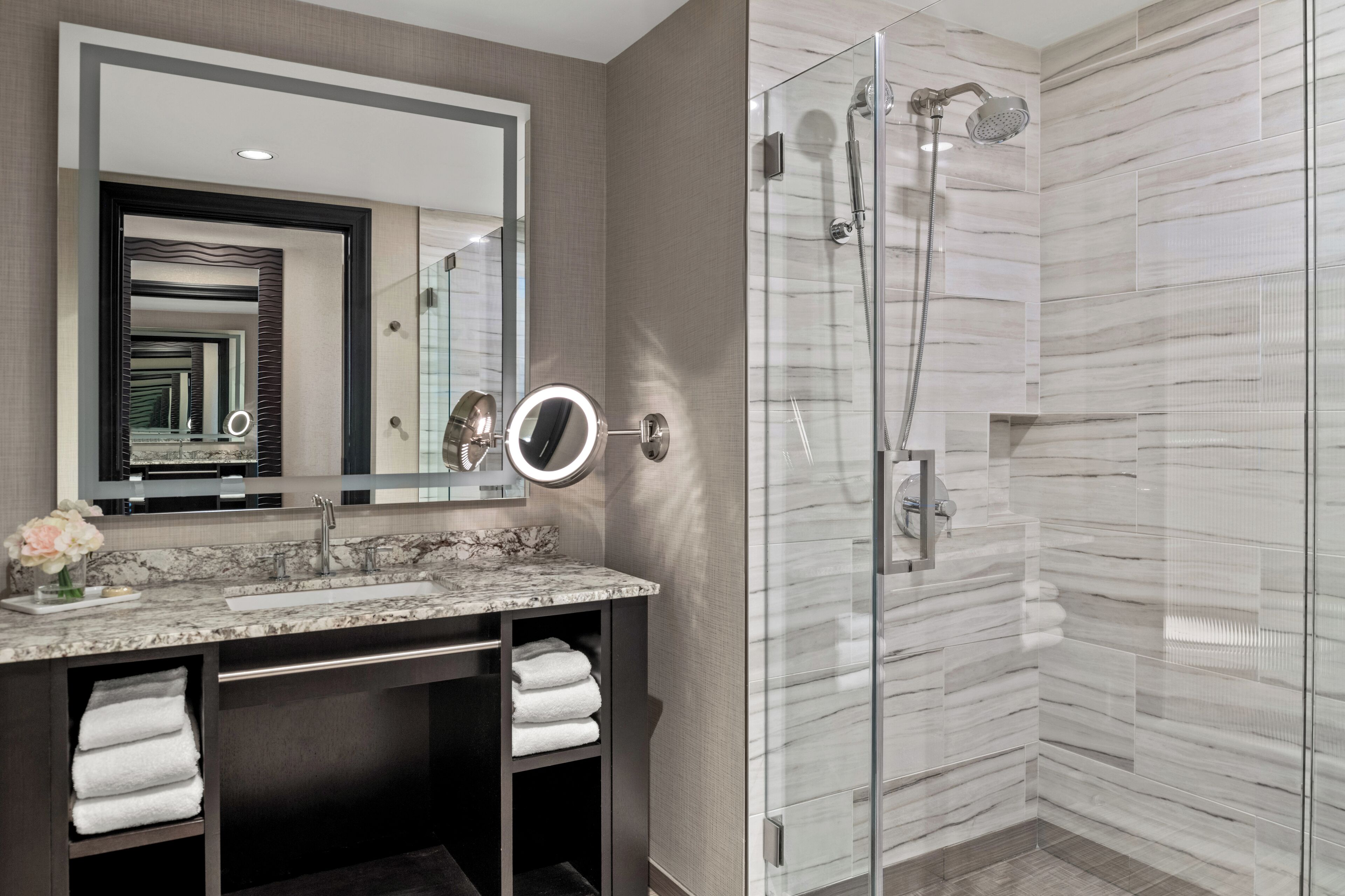 Un baño moderno con lavamanos de mármol, un espejo grande y una ducha con paredes de vidrio.