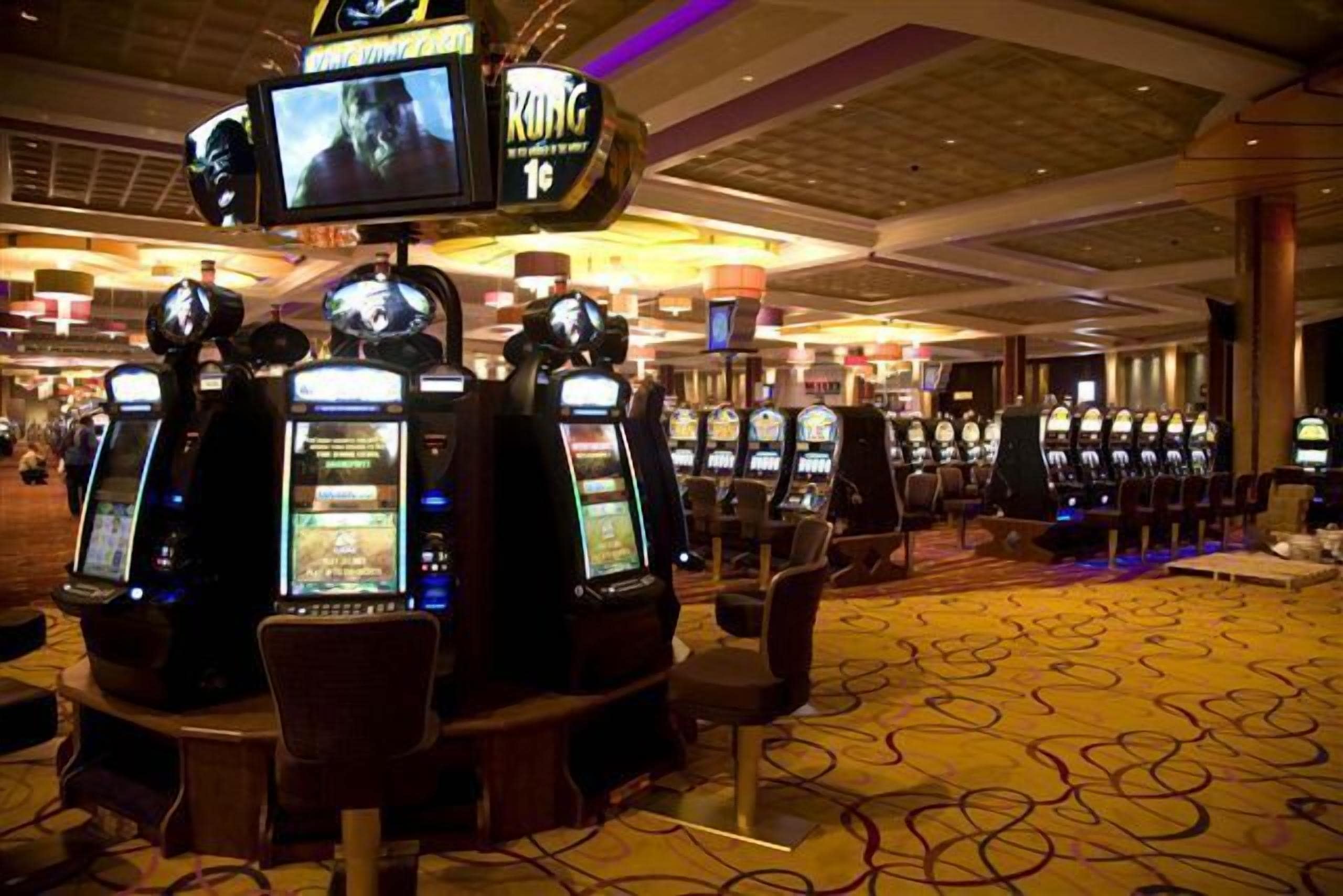 Un casino amb diverses màquines escurabutxaques i una gran pantalla que mostra una pel·lícula.