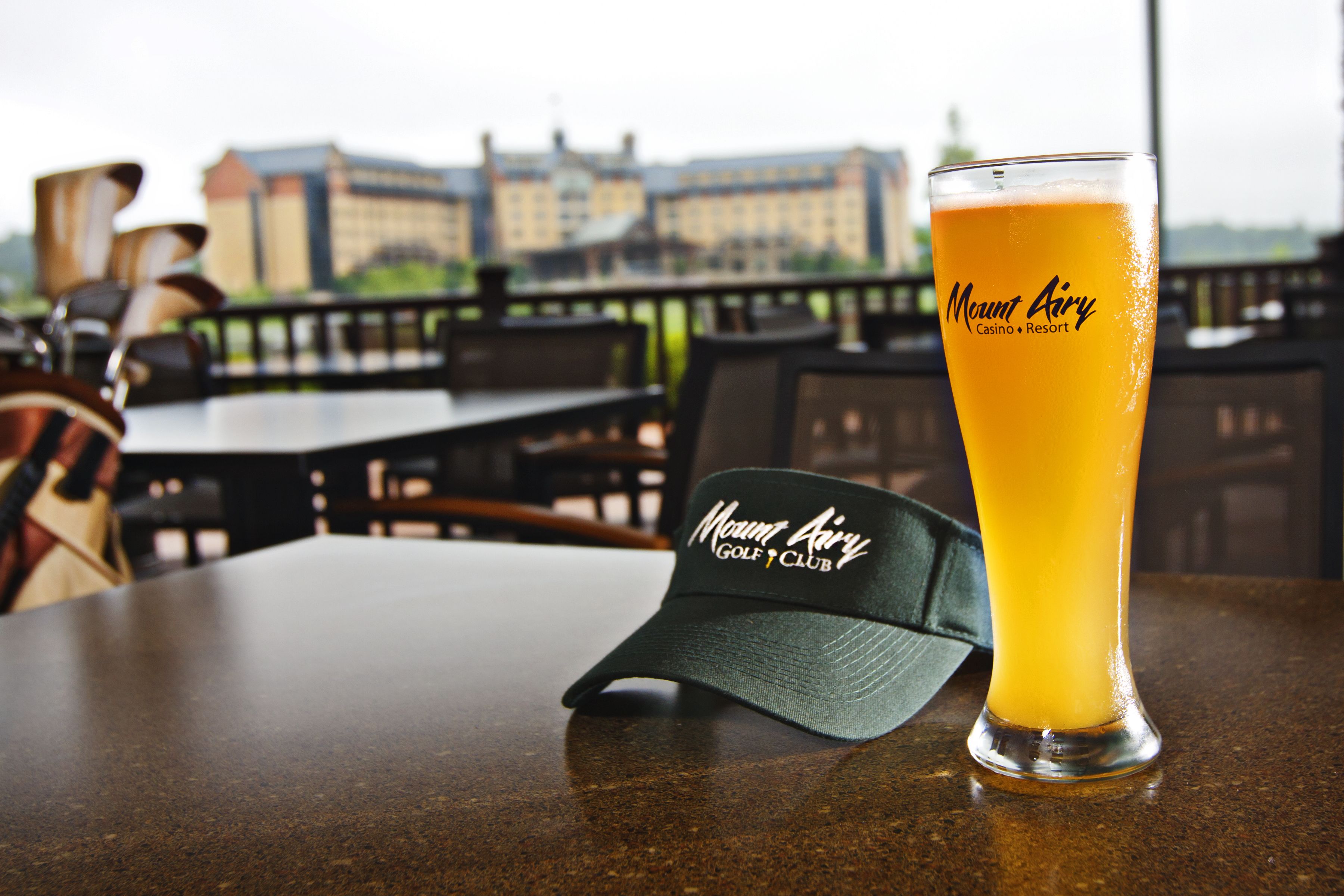 A glass of orange beverage on a table with a cap labeled "Mount Airy Golf Club".