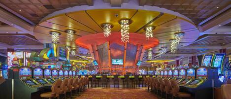 Un casino con múltiples máquinas tragamonedas, zona de bar y una gran lámpara de araña.