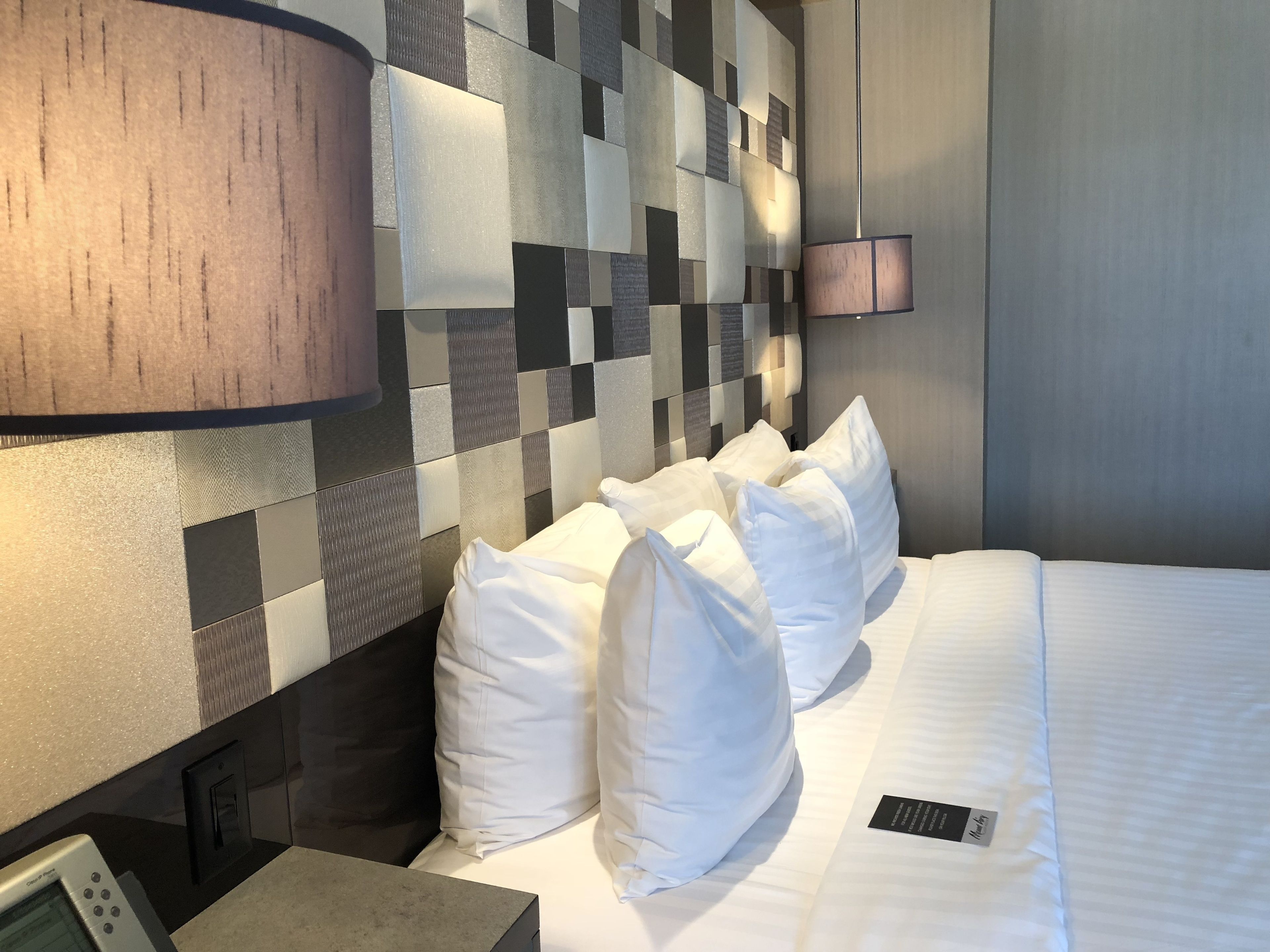 Une chambre d’hôtel avec une tête de lit à carreaux, du linge de lit blanc et une table de chevet avec une lampe.