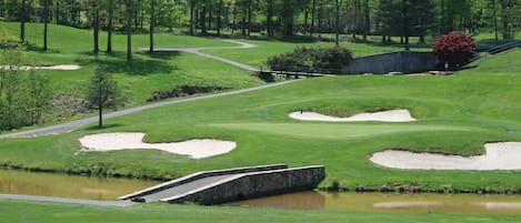A golf course with sand bunkers, a bridge, and a pond.