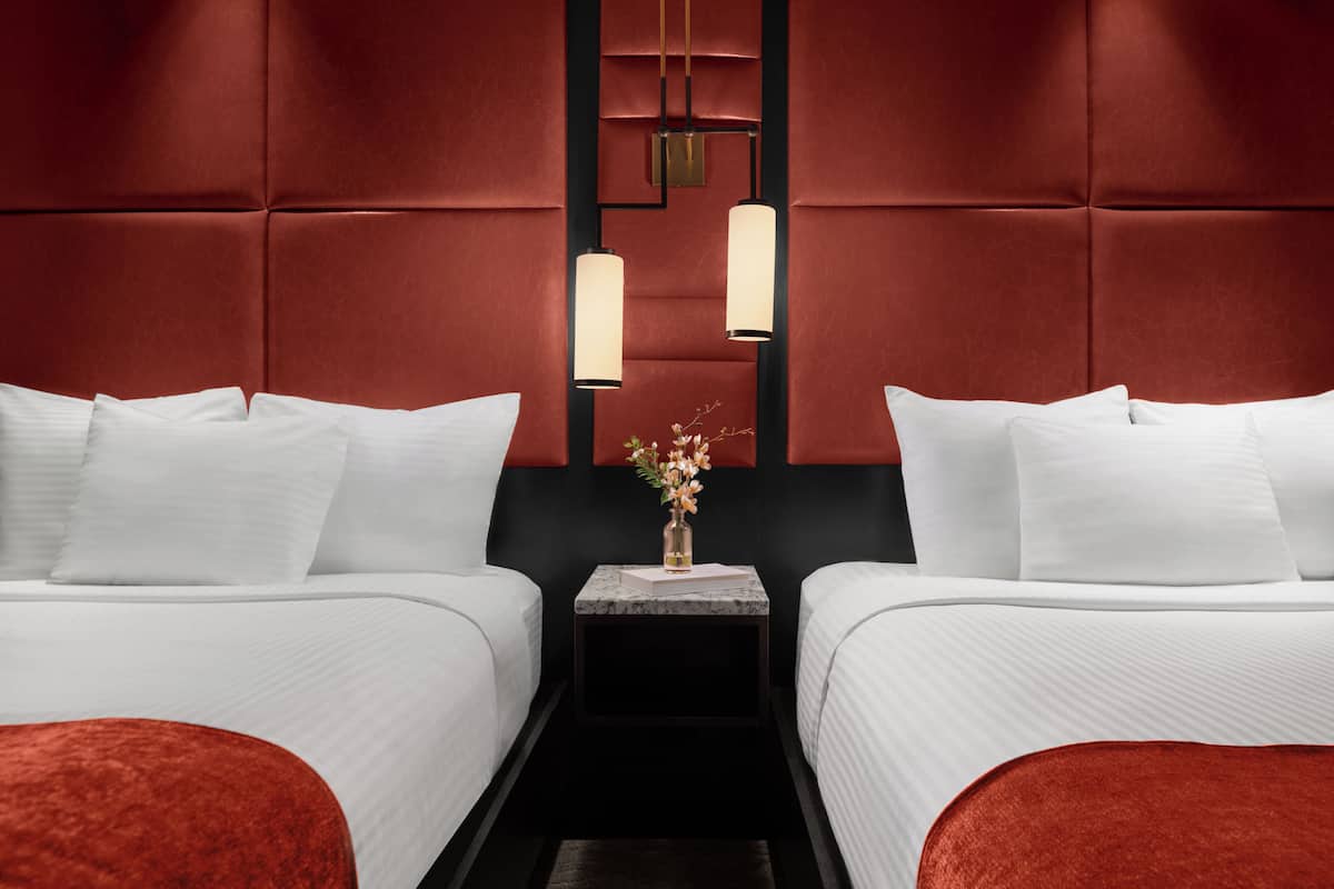 Una habitación de hotel con dos camas, una mesita de noche de mármol y un florero con flores.