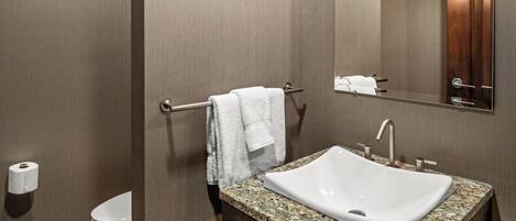 A modern bathroom with a granite countertop sink, a towel rack, a toilet, and a mirror.