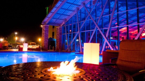 A pool area with a fire feature, lounge chairs, and a building with a glass facade.