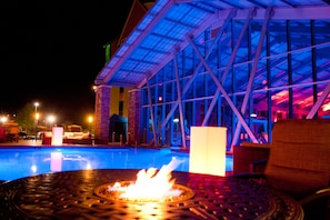 A pool area with a fire feature, lounge chairs, and a building with a glass facade. - Mount Airy Casino Resort - Adults Only 21+ (Mount Pocono)