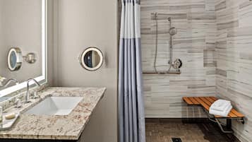 Un baño moderno con lavamanos de mármol, ducha con cabezal de lluvia y un banco con toalla.