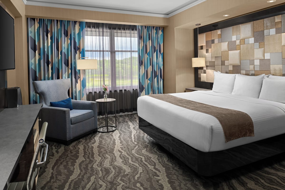 Una habitación de hotel con una cama grande, una silla, una mesita y un televisor.