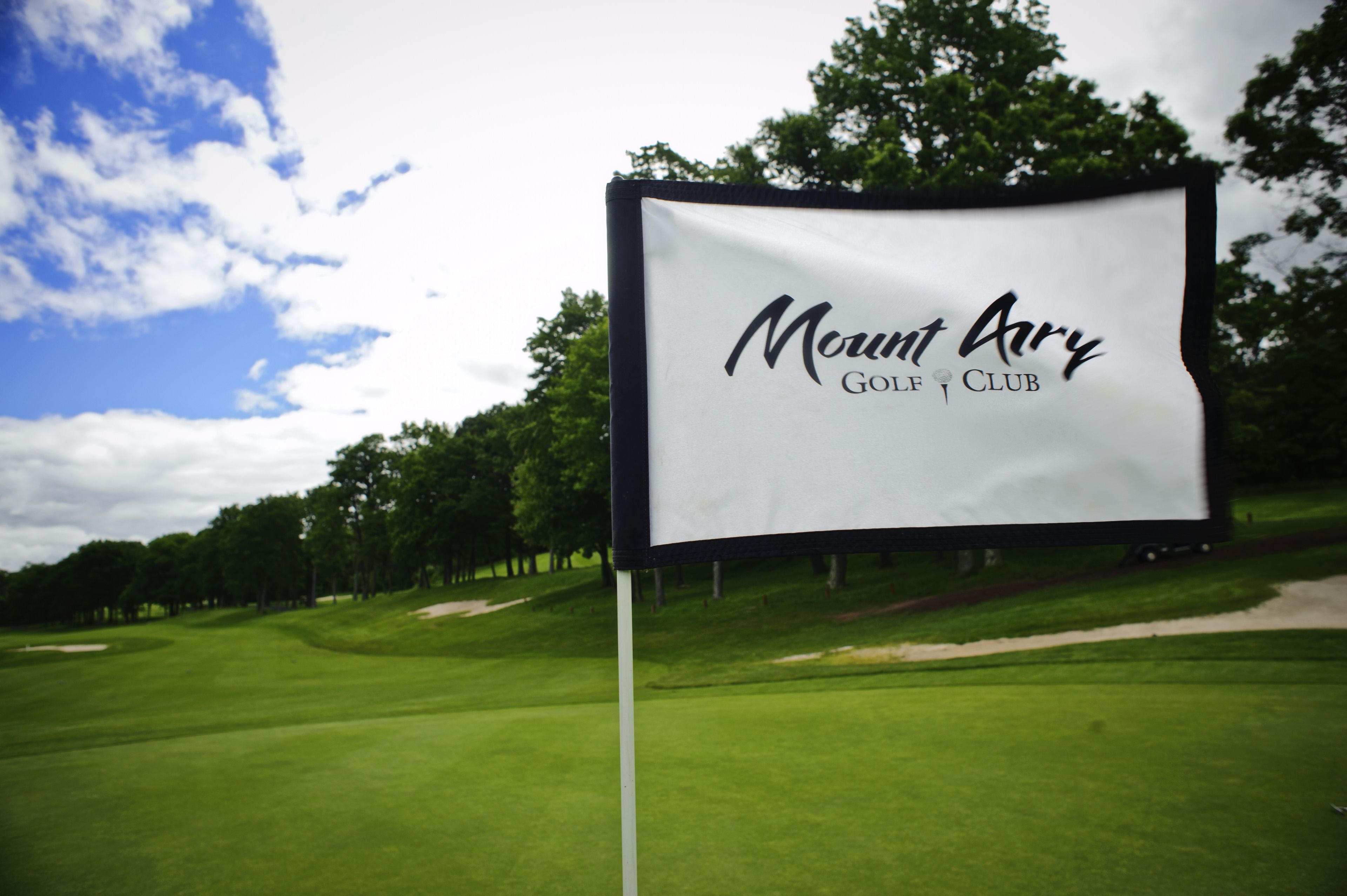 A golf club sign with the name "Mount Ary Golf Club" on a grassy field with trees in the background.