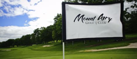 A golf club sign with the name "Mount Ary Golf Club" on a grassy field with trees in the background.