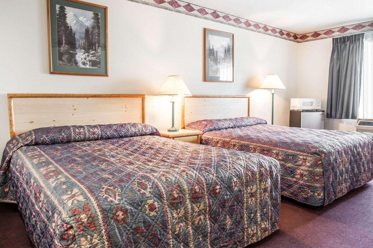A hotel room with two beds, a microwave, a lamp, and two framed pictures on the wall.