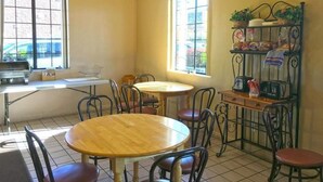 A dining area with two round tables, chairs, a metal shelf with kitchen items, and windows with a view. - America's Best Inn & Suites St. George (St. George)