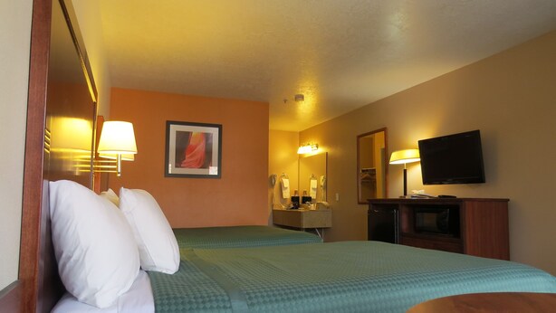 A hotel room with two beds, a wooden desk, a television, a mirror, and a wall-mounted lamp. - America's Best Inn & Suites St. George (St. George)
