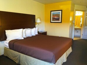 A hotel room with a large bed, a nightstand, a lamp, and a painting on the wall. - America's Best Inn & Suites St. George (St. George)