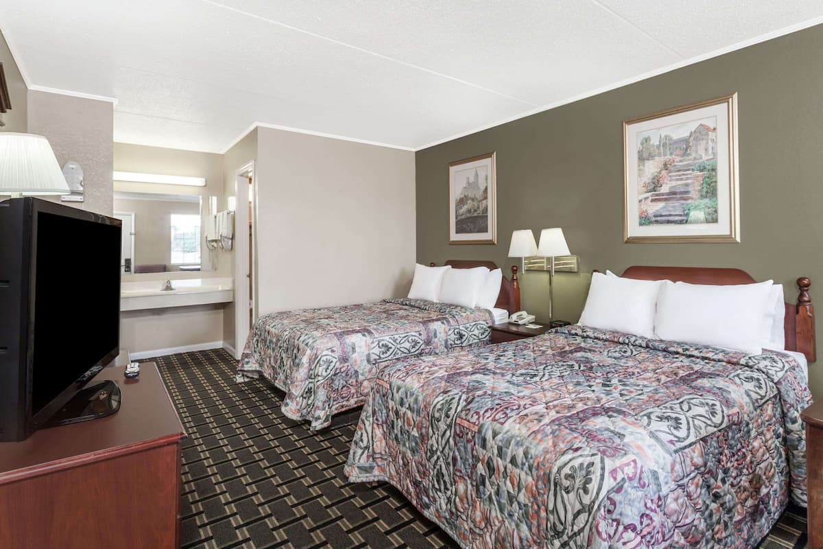Habitación de hotel con dos camas, televisión, escritorio y baño.