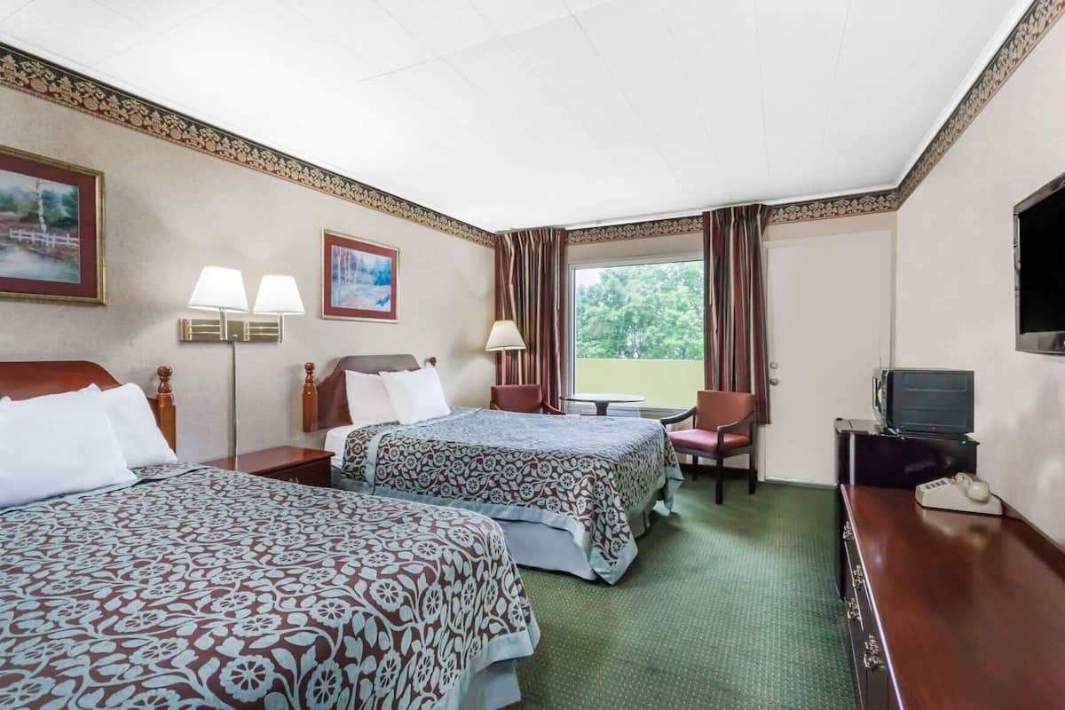 Une chambre d’hôtel avec deux lits, un bureau avec une télévision, une chaise et une fenêtre avec des rideaux.