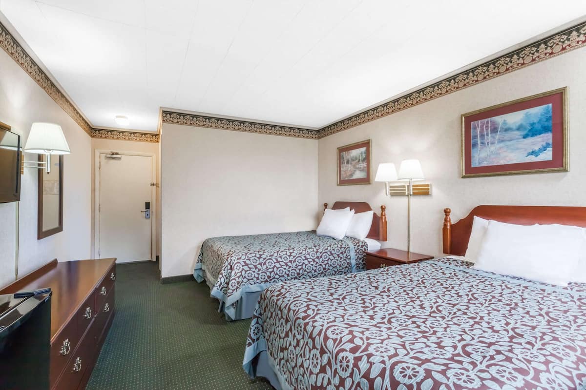 Une chambre d’hôtel avec deux lits, une commode, une lampe et un tableau au mur.