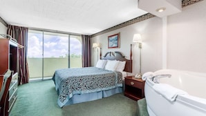 Een hotelkamer met een bed, nachtkastje, lamp, badkamer met bad en uitzicht op de omgeving.