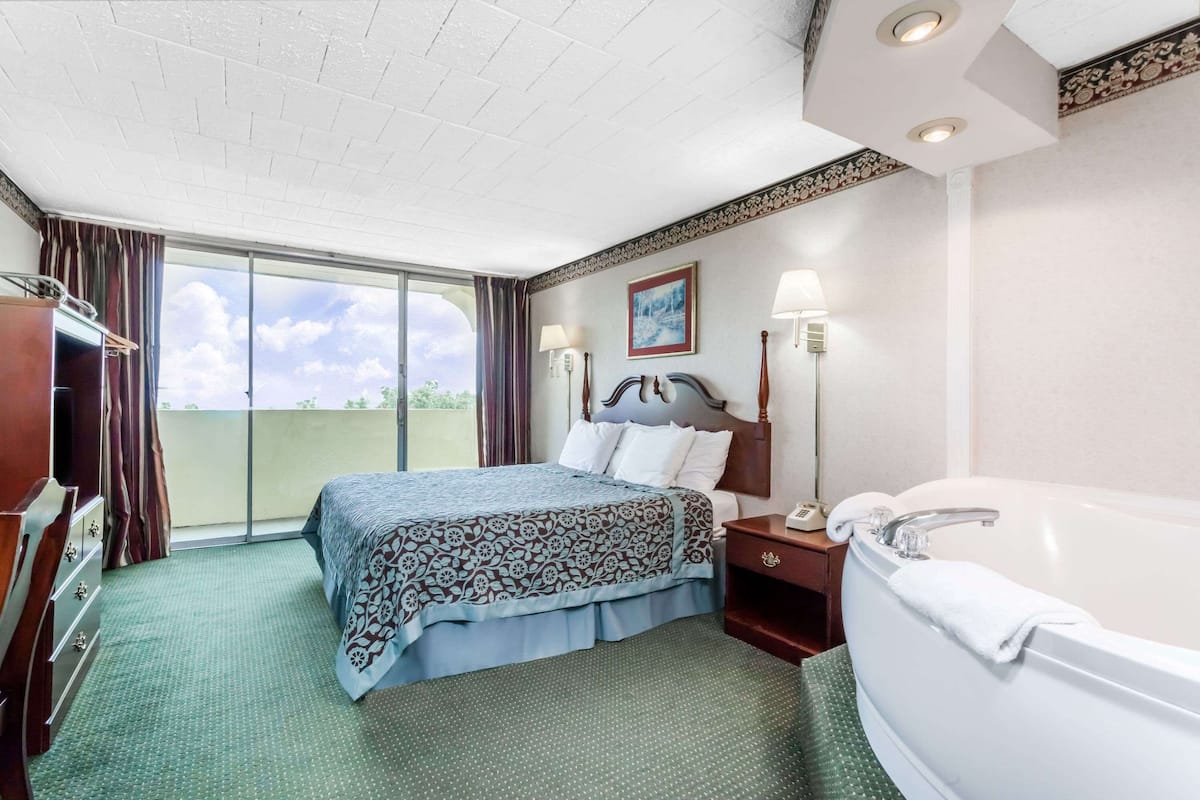 Une chambre d’hôtel comprenant un lit, une table de chevet, une lampe, une salle de bain avec baignoire et une vue sur l ’extérieur.