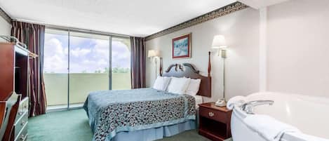 A hotel room with a bed, a nightstand, a lamp, a bathroom with a bathtub, and a view of the outdoors.