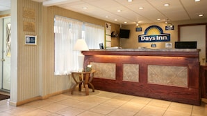 Een receptiegedeelte met een houten balie, een kleine ronde tafel met een lamp, en een bord met de tekst Days Inn.