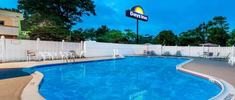 A swimming pool with a Days Inn sign, surrounded by a white fence and lounge chairs.