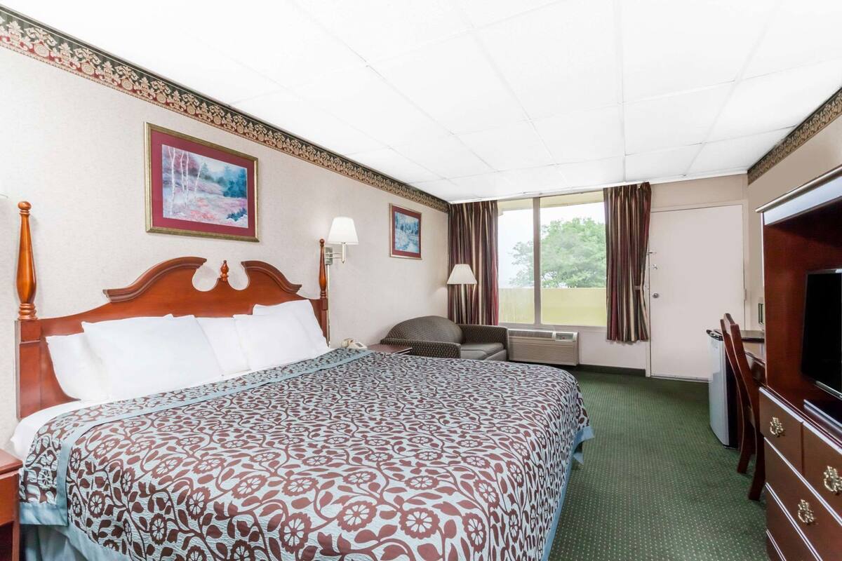 Une chambre d’hôtel avec un grand lit, un bureau, une télévision et une fenêtre avec des rideaux.