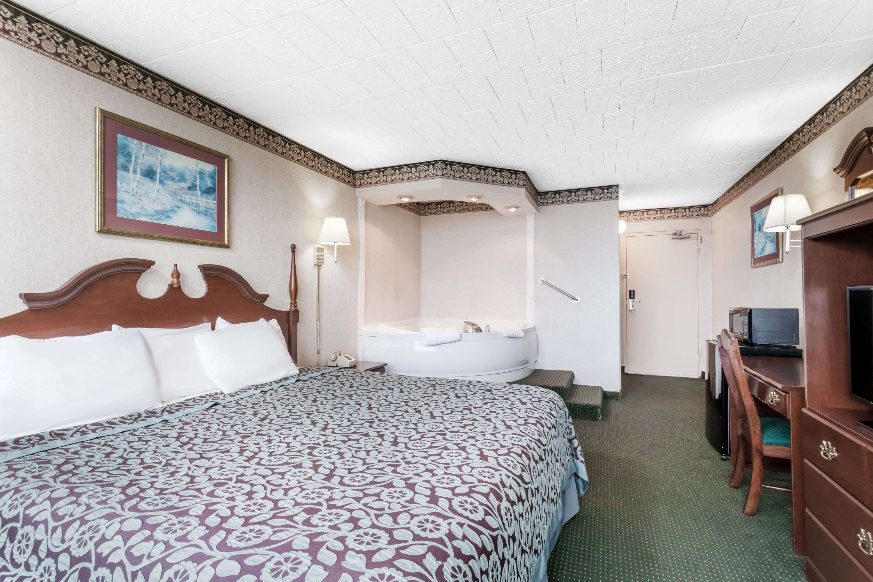 A hotel room with a large bed, a sitting area with a desk and chair, a television, and a bathtub.