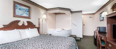 A hotel room with a large bed, a sitting area with a desk and chair, a television, and a bathtub.