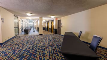 A hotel corridor with a patterned carpet, a conference table with chairs, and doors leading to rooms.