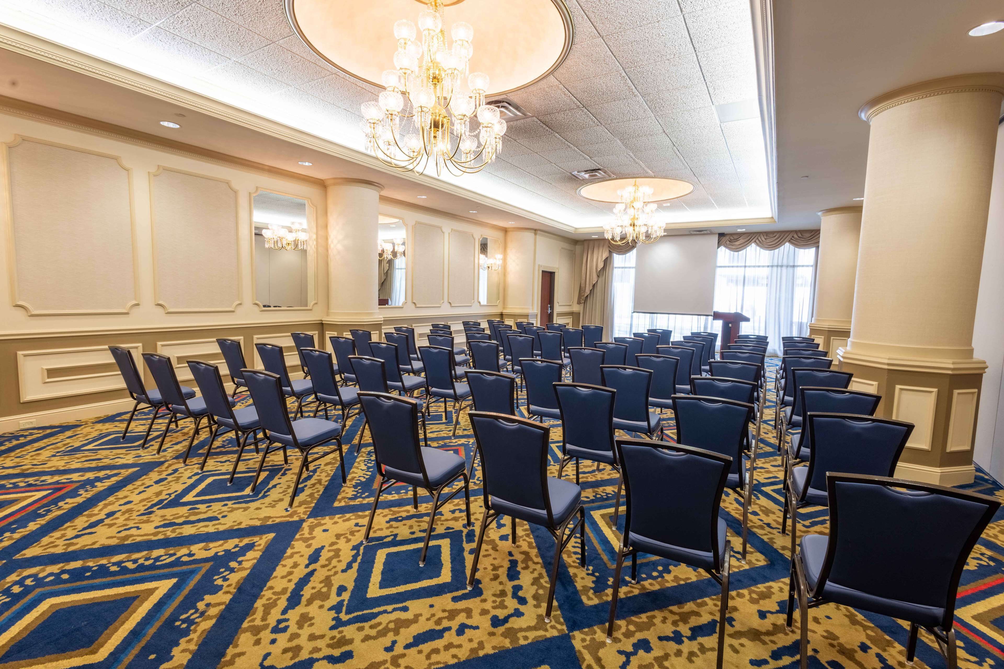A conference room with rows of chairs, a patterned carpet, and chandeliers.