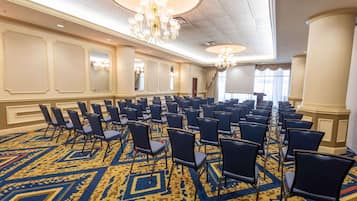 A conference room with rows of chairs, a patterned carpet, and chandeliers.