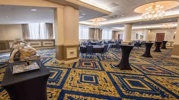 A spacious hotel lobby with a patterned carpet, round tables, and chairs, and a buffet setup.